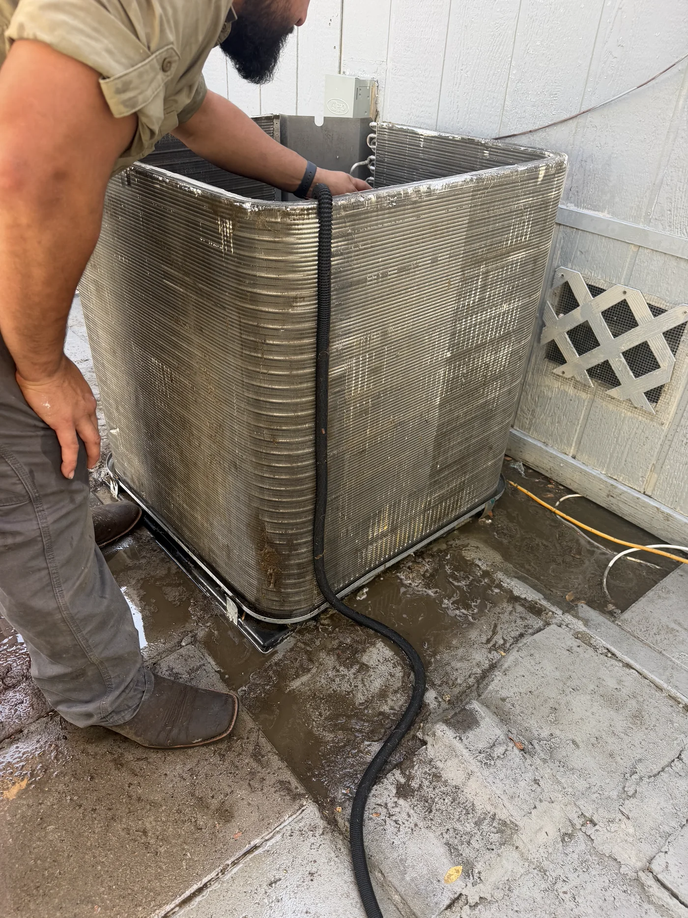 Technician cleaning an outdoor AC condenser coil during maintenance