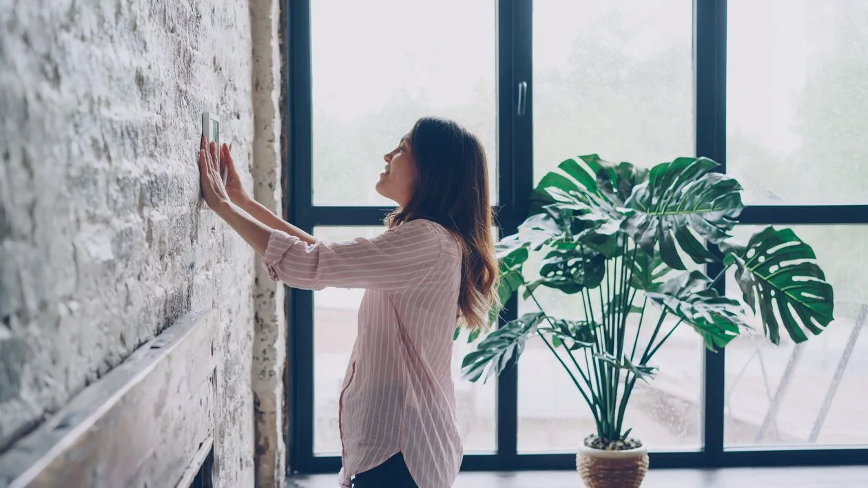 Woman adjusting a wall thermostat in a bright room